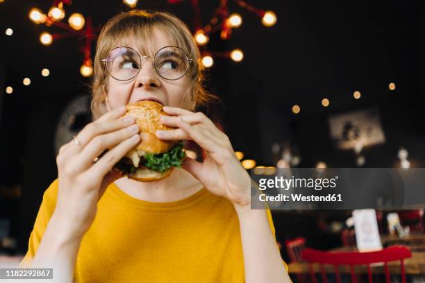 young woman eating burger in a restaurant - biting on something stock-fotos und bilder
