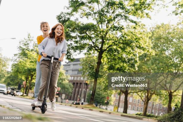 happy female friends riding e-scooter together in the city - sustainable transportation stock pictures, royalty-free photos & images