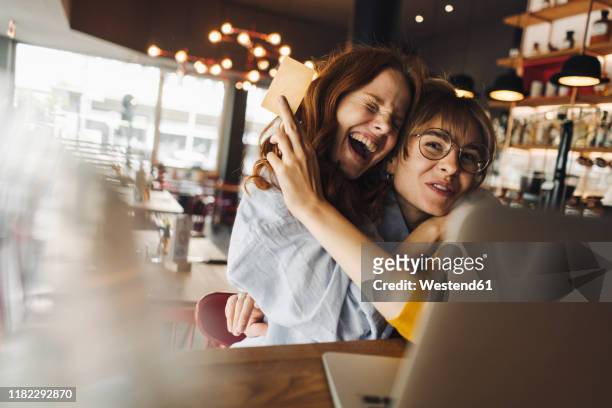 two excited female friends with laptop and credit card in a cafe - credit card stock-fotos und bilder