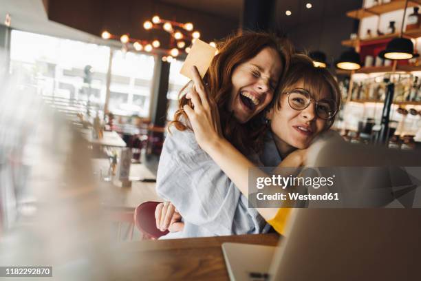 two excited female friends with laptop and credit card in a cafe - travel credit card stock pictures, royalty-free photos & images