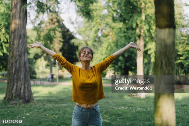 young woman in a park with outstretched arms - zufriedenheit stock-fotos und bilder