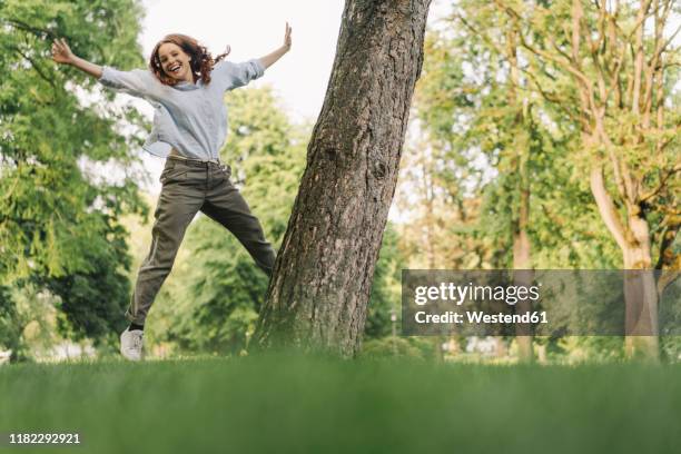 portrait of happy redheaded woman in a park - frau arme hoch ganzkörper stock-fotos und bilder