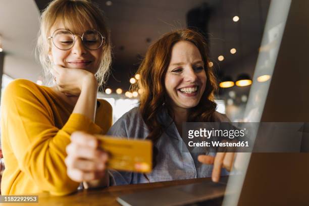 two happy female friends with laptop and credit card in a cafe - online shopping fotografías e imágenes de stock