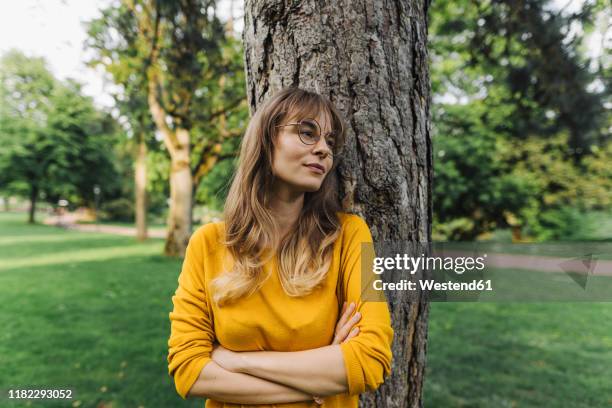 young woman at a tree in park looking sideways - leaning tree stock pictures, royalty-free photos & images