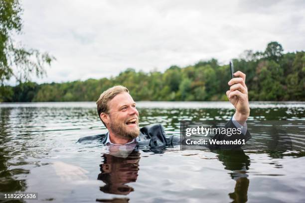 mad businessman holding cell phone inside a lake - sinking stockfoto's en -beelden