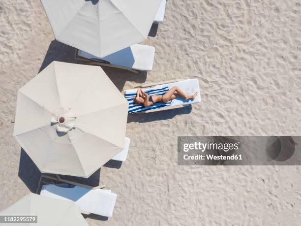 woman lying on sun lounger at the beach, gili air, gili islands, indonesia - umbrellas from above stockfoto's en -beelden