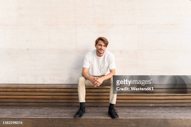 portrait of smiling man sitting on wooden bench - bench foto e immagini stock