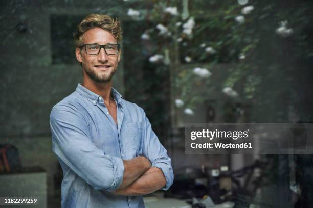 portrait of casual young businessman behind windowpane in office - portrait business man stock-fotos und bilder