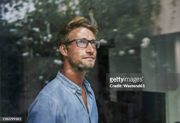 casual young businessman behind windowpane in office - beschaulichkeit stock-fotos und bilder