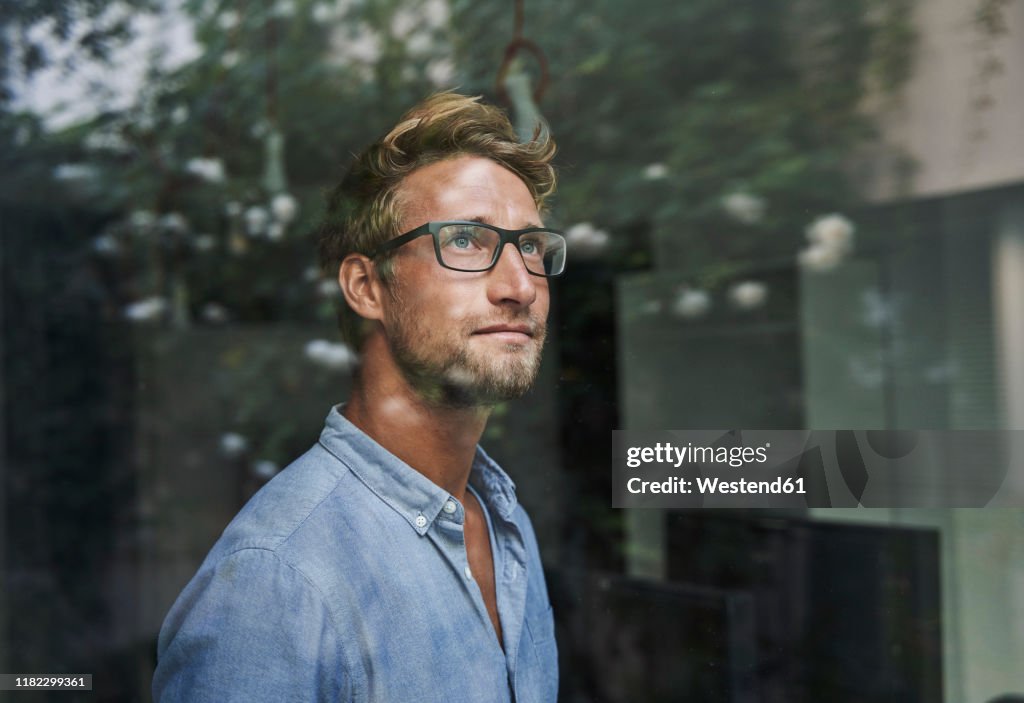 Casual young businessman behind windowpane in office