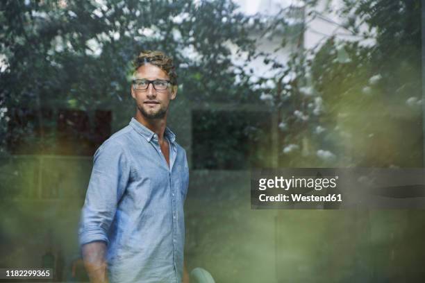 casual young businessman behind windowpane in office - reflection stock-fotos und bilder