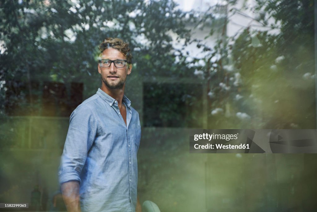 Casual young businessman behind windowpane in office