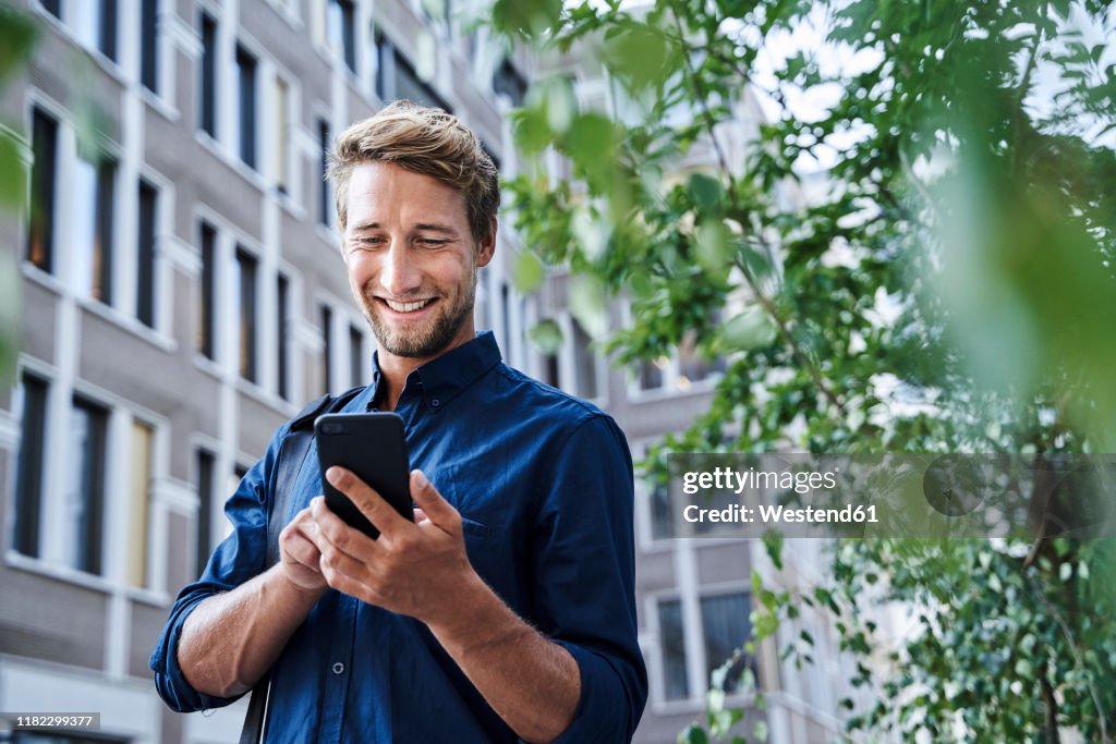 Smiling young businessman using mobile phone in the city