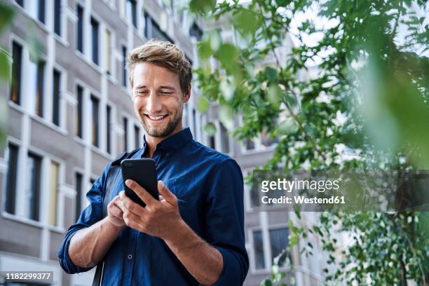 smiling young businessman using mobile phone in the city - photo call stock-fotos und bilder