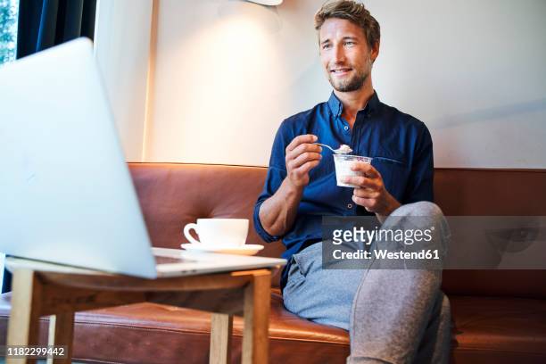 young businessman eating and using laptop in a cafe - blaues hemd stock-fotos und bilder