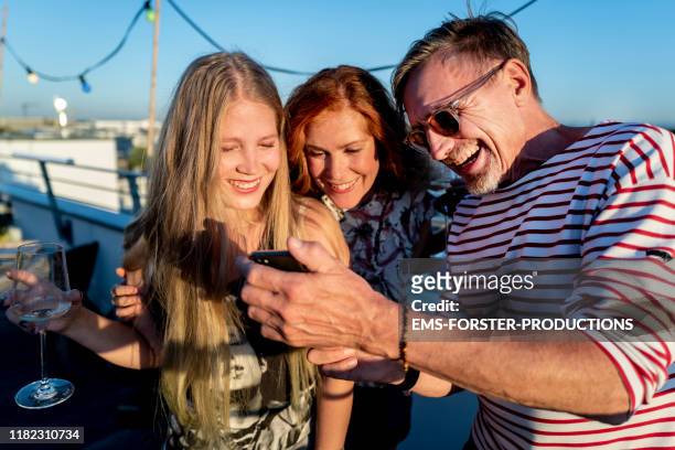 group of friends looking at smartphone on a urban rooftop - cliqueimages stock pictures, royalty-free photos & images