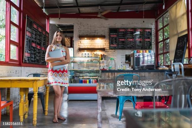 Young woman business owner with laptop standing in her coffee shop