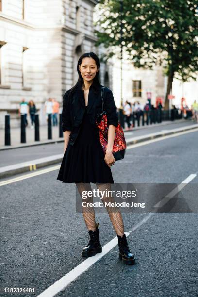 Model Heejung Park wears a black jacket, black dress, red tartan tote bag, fishnet tights, and black Doc Marten boots after the Halpern show during...