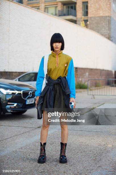 Model Ruinan Dong wears a green and blue Acne Studios windbreaker top, green skirt, and black boots after the Preen by Thornton Bregazzi show during...