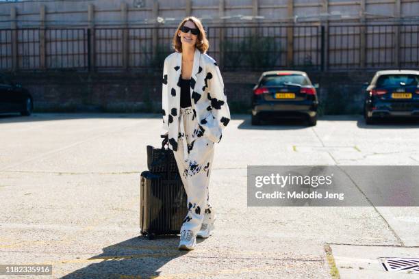 Model Lena Hardt wears a Lemaire white splotched suit, white sneakers, black Paco Rabanne bag, and black Rimowa rolling suit case after the Preen by...