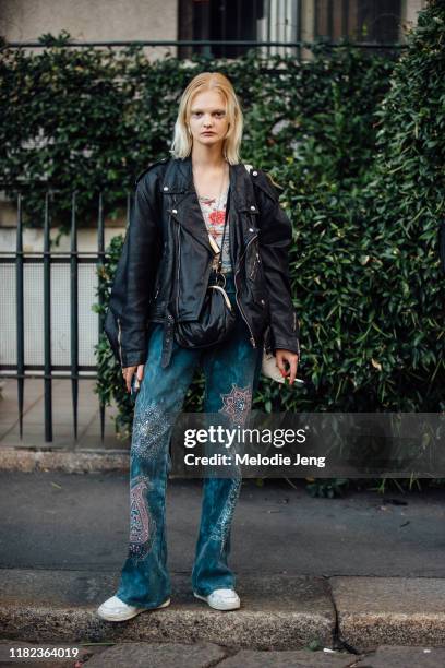 Model Unia Pakhomova wears a black leather jacket, black purse, blue paisley embellished jeans, and white sneakers after the Marco de Vincenzo show...