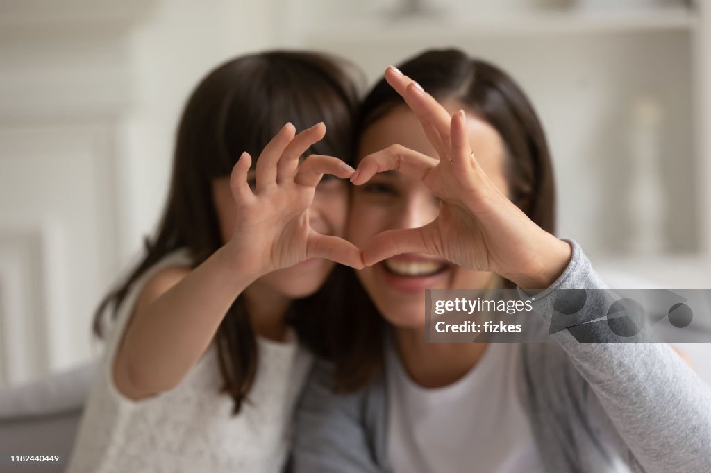 Happy young mother with little daughter making focused heart sign.