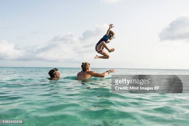 5 year old son on mother's shoulders leaping into the ocean at sunset - caribbean sea life stock pictures, royalty-free photos & images