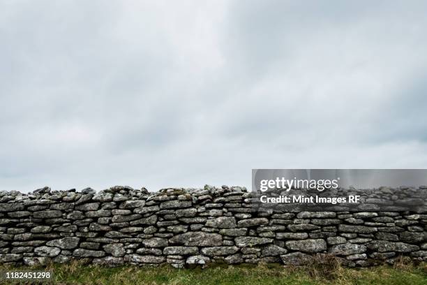 view of old dry stone wall under a cloudy sky. - stenen muur stockfoto's en -beelden