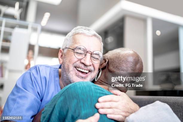 male nurse embracing a patient at home - male nurse hug stock pictures, royalty-free photos & images