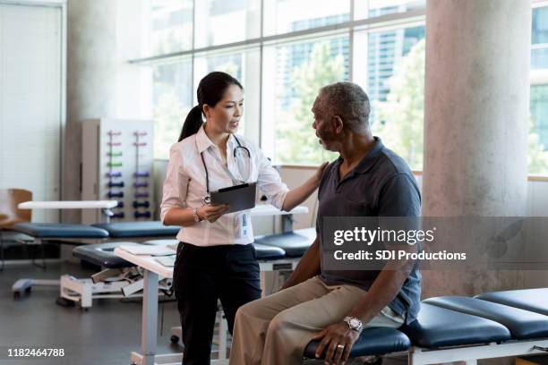 female physical therapist assesses a mature adult male patient - rehabilitation center stock pictures, royalty-free photos & images