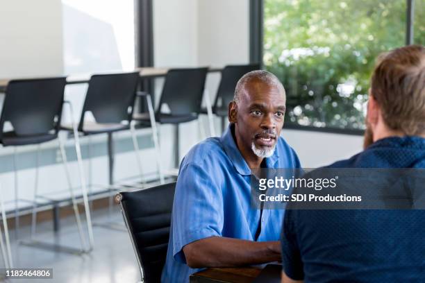 mature man interviews unrecognizable man for job in small business - serious interview stock pictures, royalty-free photos & images