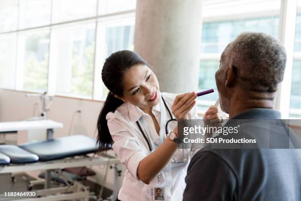 female doctor examines a senior man's throat - tongue depressor stock pictures, royalty-free photos & images