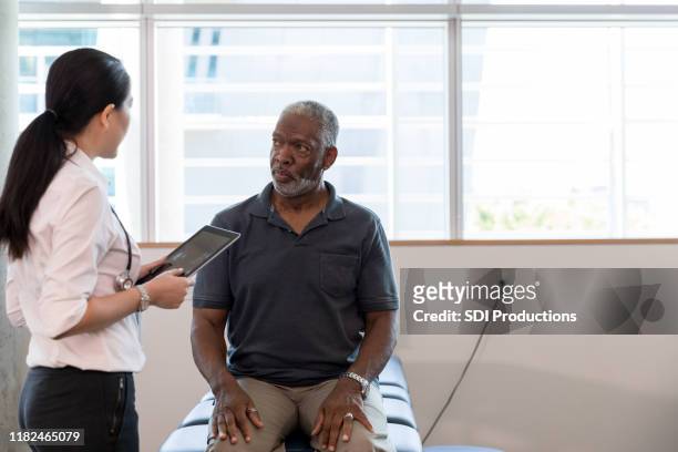 therapist uses digital tablet to diagnose mature patient's problem - outpatient care stock pictures, royalty-free photos & images