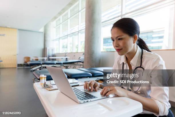 mid adult female doctor uses laptop in physical therapy room - physiotherapy asian stock pictures, royalty-free photos & images