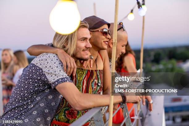 three friends are enjoying a summer party on a urban rooftop in munich and looking into an amazing sunset - lichterkette sommer stock-fotos und bilder