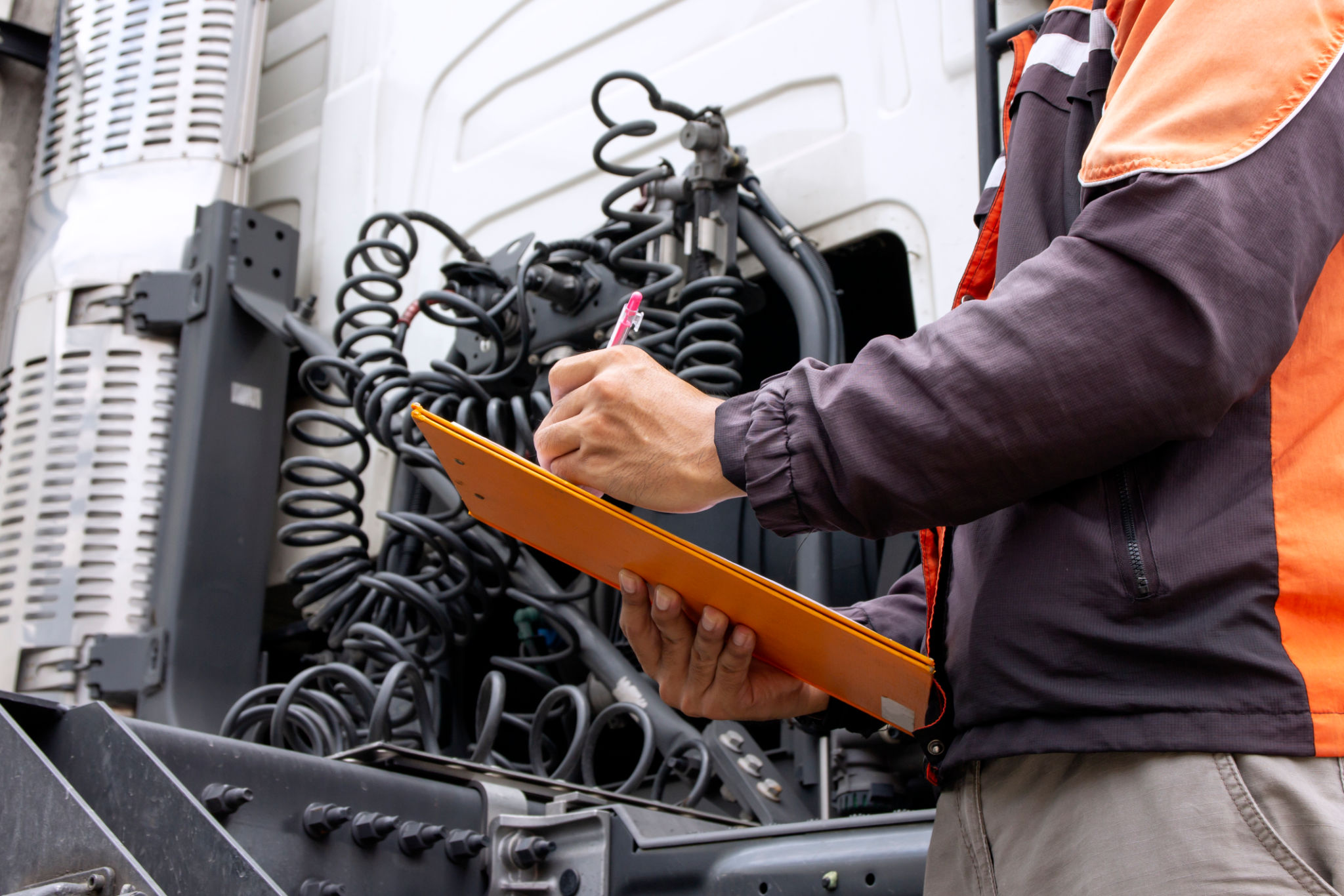 Truck driver holding clipboard inspecting safety daily check the engine of semi truck Truck driver holding clipboard inspecting safety daily check the engine of semi truck