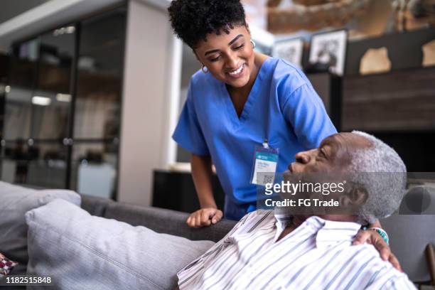 female nurse taking care of a senior man at home - person of colour stock pictures, royalty-free photos & images