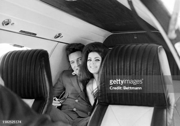 Singer Elvis Presley peeks out from behind his wife, Priscilla Ann Beaulieu, as the couple sit in a chartered jet airplane after their wedding at the...