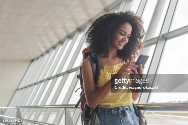 giovane donna con zaino controllando il suo programma di imbarco in aeroporto - aeroporto foto e immagini stock