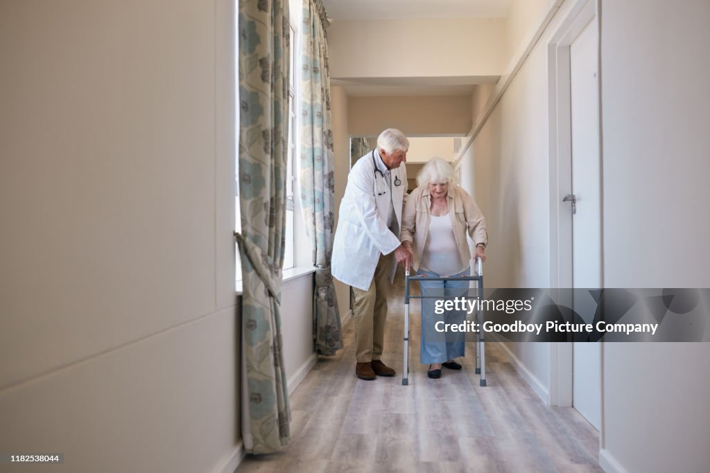 Doctor helping his elderly patient use her walking frame