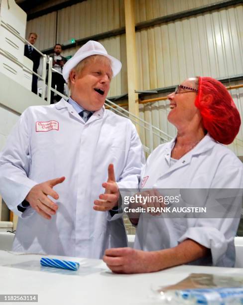 Britain's Prime Minister Boris Johnson shares a joke with a worker as he assists in the production of candy sticks during a visit to Blackpool rock...