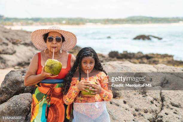 ブラジルの熱帯ビーチでココナッツウォーターを飲む祖母と孫娘 - 2 coconut drinks ストックフォトと画像