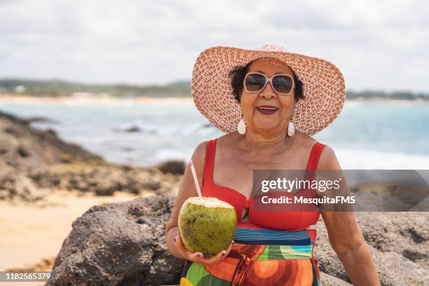 porträt einer frau, die kokoswasser trinkt - old woman in swimsuit stock-fotos und bilder