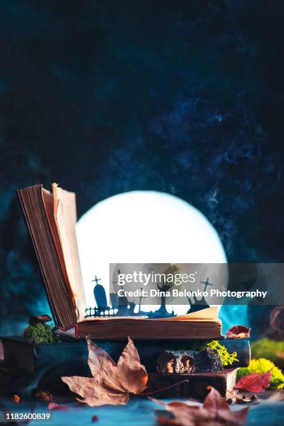open book with silhouettes of graveyard and zombie hands with full moon. halloween still life with magical book, creative and funny horror concept - open casket stock-fotos und bilder