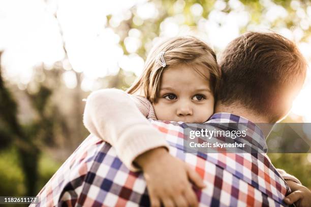 sad little girl being consoled by her single father in nature. - family sadness stock pictures, royalty-free photos & images