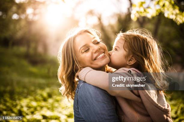 gelukkige alleenstaande moeder genieten in kus door haar dochter in het park. - friends kissing cheeks stockfoto's en -beelden