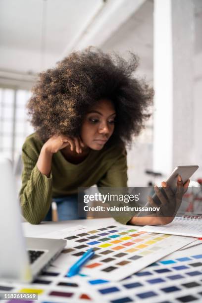 african fashion designer working in studio and using laptop and smart phone - graphic design studio stock pictures, royalty-free photos & images