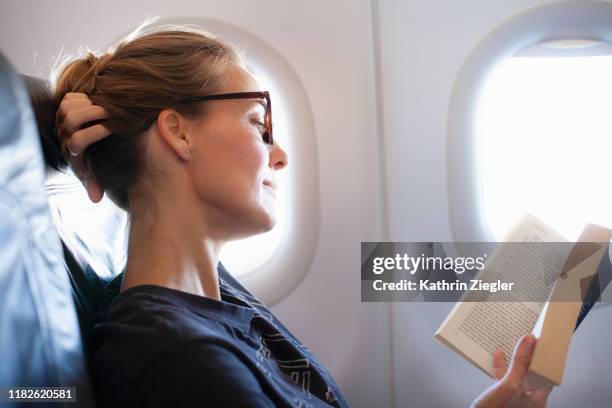 woman reading a book on airplane - lesebrille stock-fotos und bilder