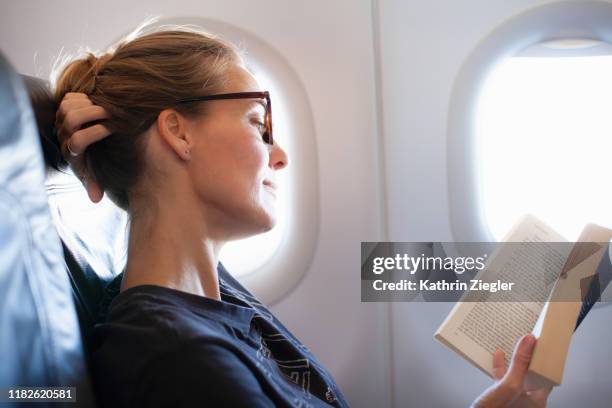 woman reading a book on airplane - reading glasses imagens e fotografias de stock