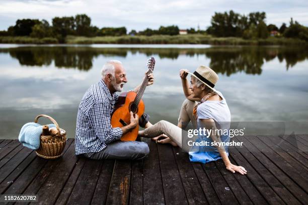 happy senior man playing a guitar to his wife on a pier in nature. - couple jetty stock pictures, royalty-free photos & images